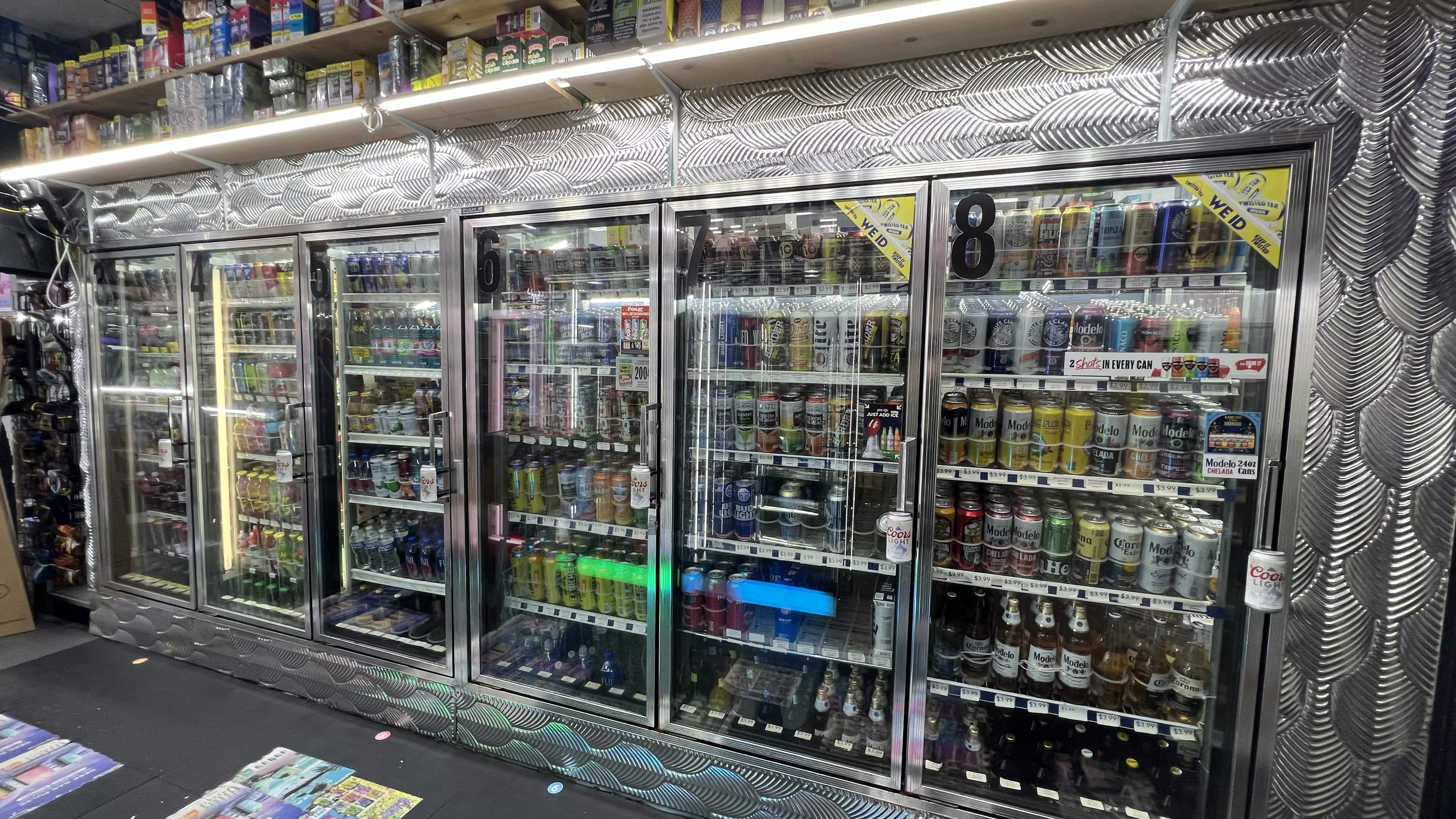 Row of glass-door coolers stocked with beer, seltzers and Modelo inside Tobacco Brew & Chew