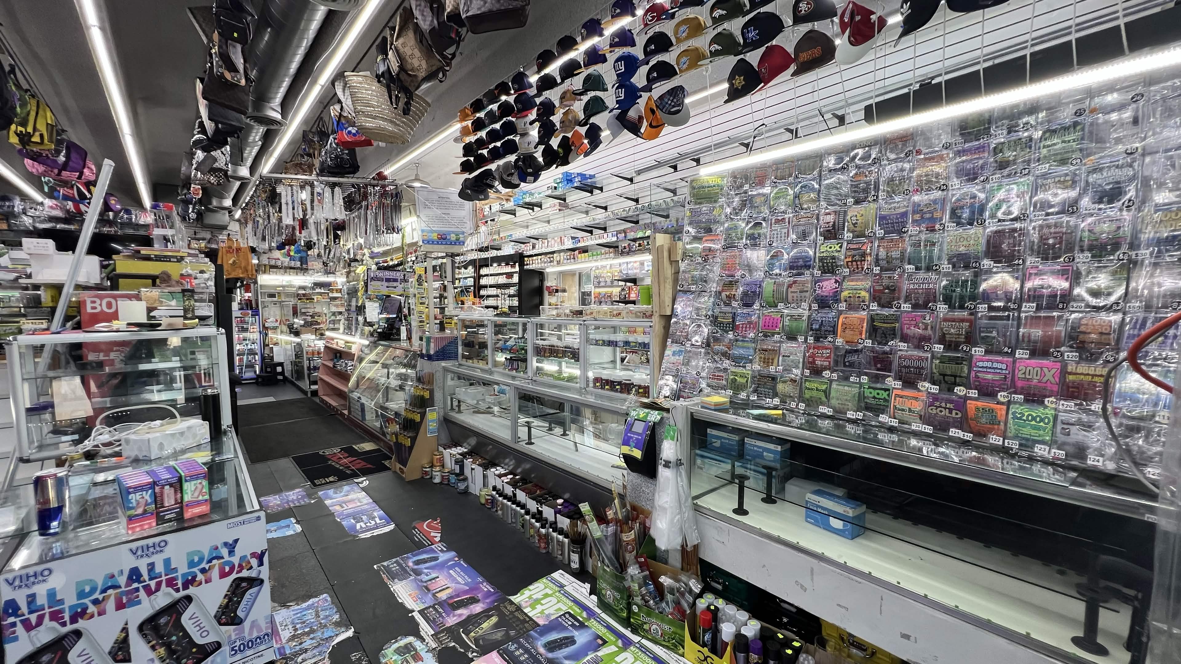 Front counter with a full wall of scratch-off lottery tickets and fitted hats inside Tobacco Brew & Chew